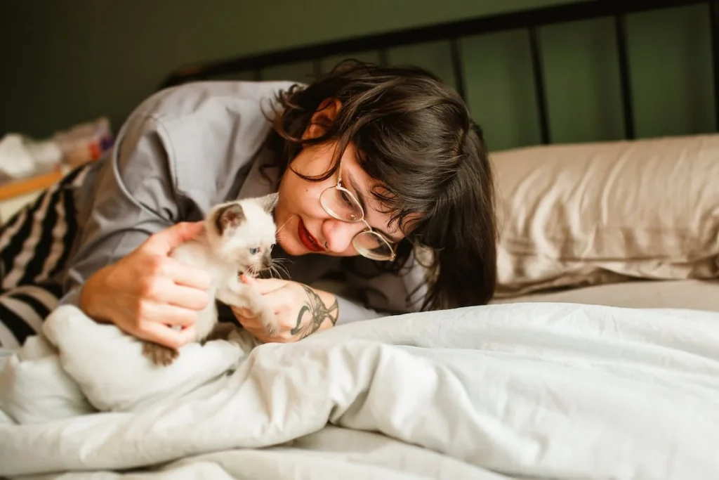 Woman cuddling a Siamese kitten on a bed — spending time with individual cats helps allergy sufferers test their reaction
